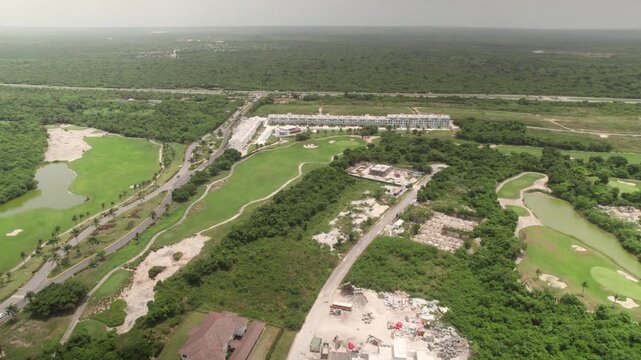 High-angle aerial drone view of a sprawling golf course, modern resort apartments, and surrounding tropical infrastructure in a coastal development in Punta Cana