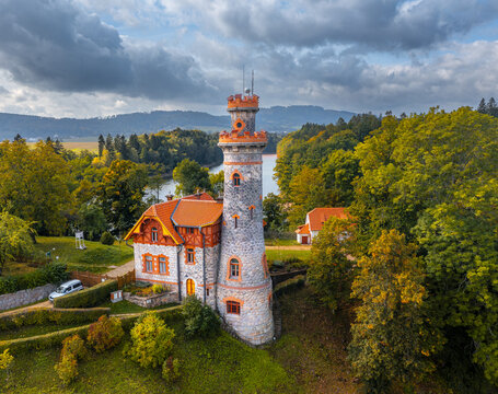 Aerial view of the Royal Forest Dam stone tower and house surrounded by autumn forest and reservoir under a cloudy sky in Bila Tremesna, Hradec Kralove Region, Czechia.