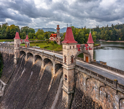 Aerial view of the historic Royal Forest Dam with its stone towers and red roofs overlooking the reservoir and lush green forests in Bila Tremesna, Hradec Kralove Region, Czechia.