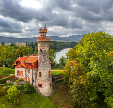 Aerial view of the historic stone tower and neo-Gothic house of the Royal Forest Dam surrounded by lush greenery and a reservoir in Bila Tremesna, Hradec Kralove Region, Czechia.