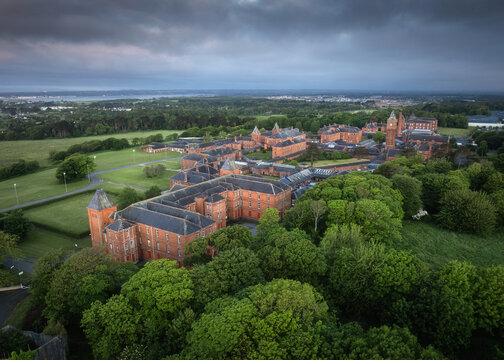 Aerial view of the historic red-brick St. Ita's Hospital surrounded by lush green trees and expansive fields in Portrane, County Dublin, Ireland.