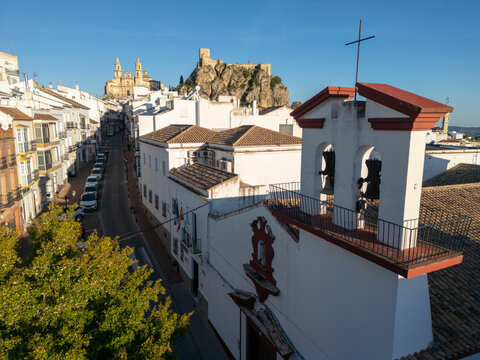 Aerial view of the historic white-washed buildings, the Parroquia de Nuestra Senora de la Encarnacion, and the Arab Castle under a clear blue sky in Olvera, Andalusia, Spain.
