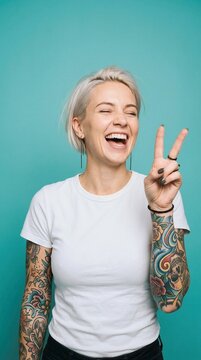 Laughing woman with tattoos making peace sign against teal background