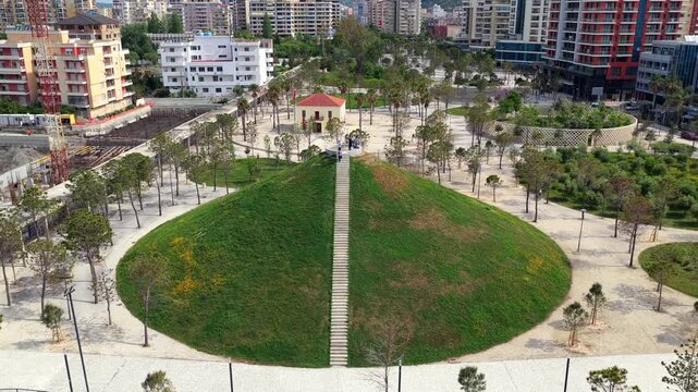 Aerial video of a contemporary urban park in Vlora, Albania, featuring a large green grass pyramid structure with stairs