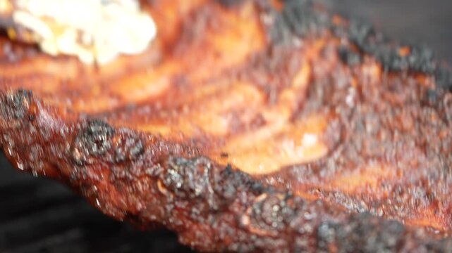 Close-up video of grilled ribs on a barbecue grill, showcasing the juicy and charred texture of the meat.
