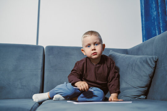 Small child sits on sofa and looks at camera in living room during daytime