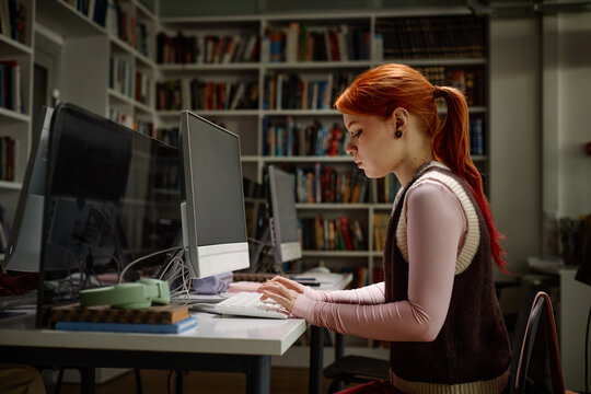 Student studying at desktop computer in library, typing research notes for schoolwork. Education concept for academic success, e learning, exam preparation
