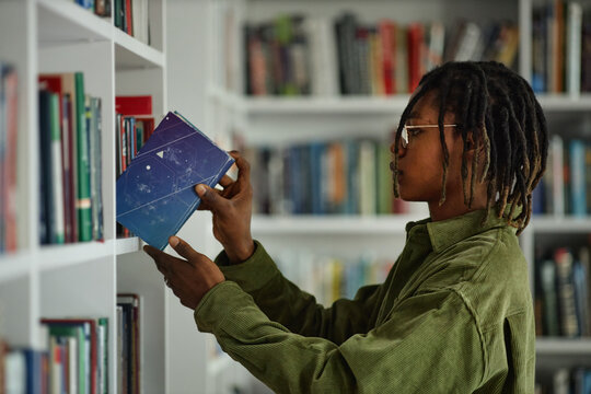Black man selecting book from library shelf, studying and researching for college assignment
