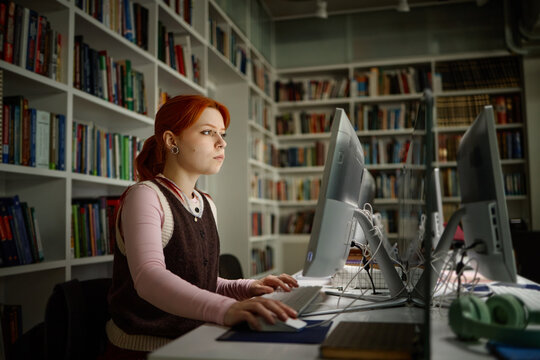 Caucasian woman studying on desktop computer in library, researching coursework and building digital skills
