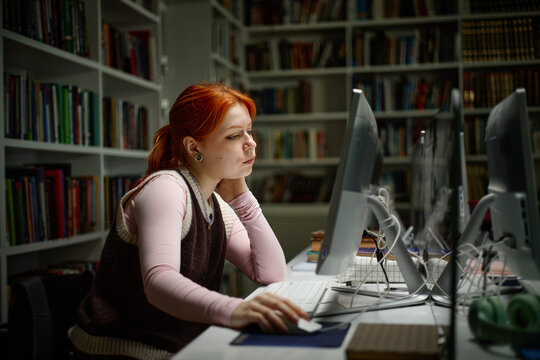 Woman studying on desktop computer in library, researching coursework and online resources
