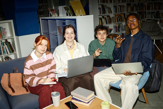 Portrait of diverse students studying with laptops and notes in library, collaborating on group project and digital learning
