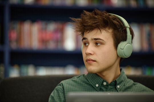 Caucasian man wearing headphones, studying with laptop in library, listening to online lesson. Education marketing, e learning, student life, close up

