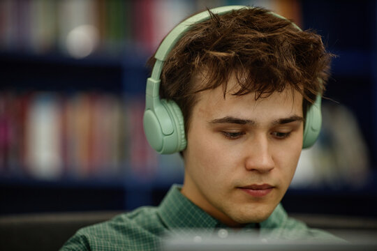 Close up of Caucasian man studying with tablet and headphones in library, focusing on online learning and concentration. Useful for education, edtech, student success
