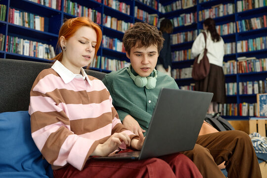 Caucasian people studying with laptop in library, researching coursework and collaborating on assignment. Education marketing, e learning, academic success concept, medium shot
