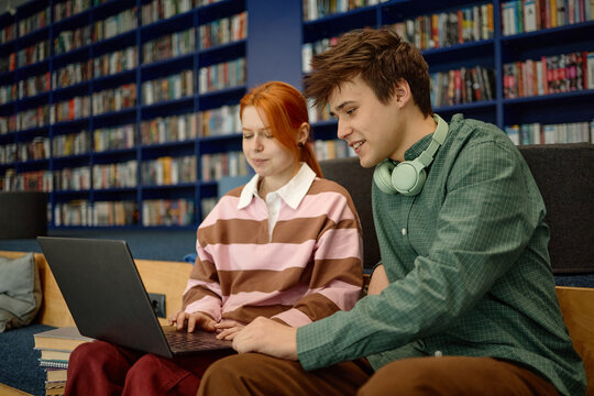 Students collaborating on laptop in library, researching coursework and studying together. Education teamwork concept for school marketing, e learning, academic support
