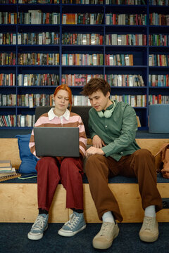 Young adult students collaborating on laptop in library, researching coursework and sharing ideas. Education technology concept for school marketing, e learning, academic support
