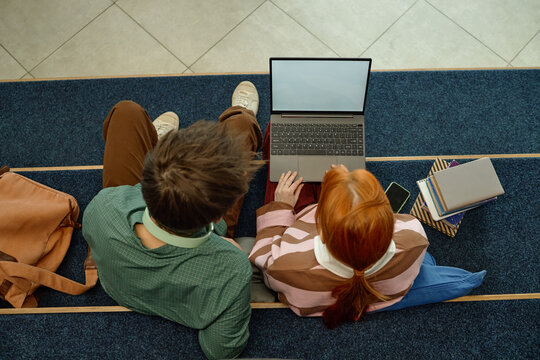 Overhead shot of anonymous students studying with laptop and books on campus steps, collaborating on coursework and digital learning
