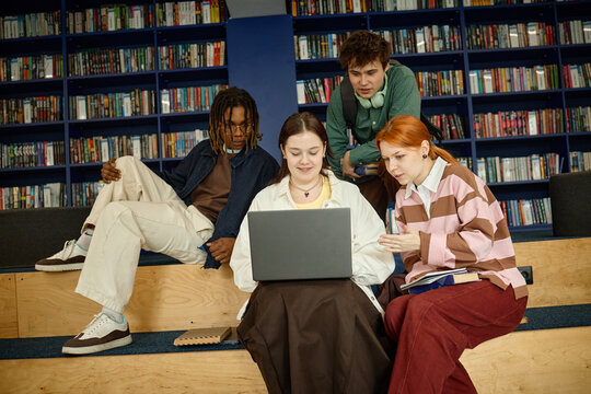 Multiethnic students collaborating on laptop in library, researching coursework and sharing ideas. Education marketing, student teamwork, digital learning, medium shot
