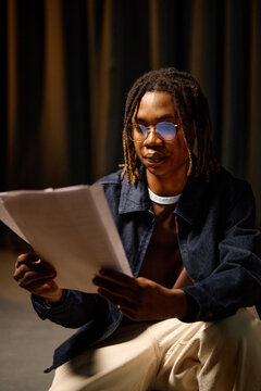 Vertical shot of African American student reading printed pages and reviewing school assignment. Education concept for exam prep, academic success, tutoring promotion
