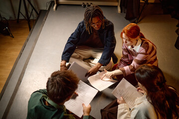 High angle view of diverse students reviewing scripts on floor, collaborating in study group or drama class. Education, teamwork, youth learning campaign or school promotion use