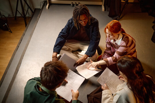 High angle view of diverse students reviewing scripts on floor, collaborating in study group or drama class. Education, teamwork, youth learning campaign or school promotion use
