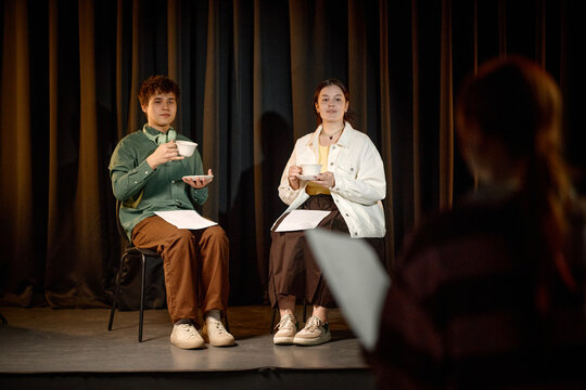 Students rehearsing stage performance while holding cups and scripts, practicing public speaking and drama skills. Useful for education, theater workshop, youth training marketing
