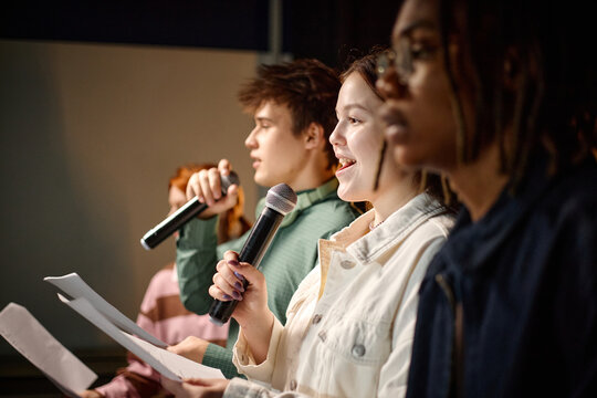 Biracial students speaking into microphones and reading notes during school presentation, showing public speaking and teamwork. Useful for education marketing, student leadership campaigns
