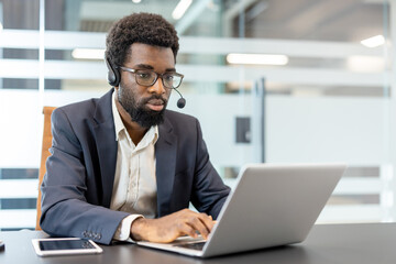 Young male employee providing customer service assistance, actively typing on a laptop with a...