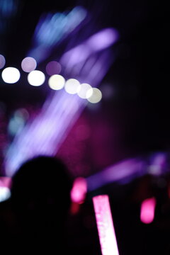 Abstract colorful concert bokeh background with blurred stage lights and glowing pink light stick silhouette, creating an energetic nightlife and live music atmosphere with soft defocused illumination