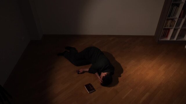 Man lying on a wooden floor in a dimly lit room, holding a sacred scripture, symbolizing a moment of deep grief, spiritual struggle, and profound prayer, seeking comfort and connection