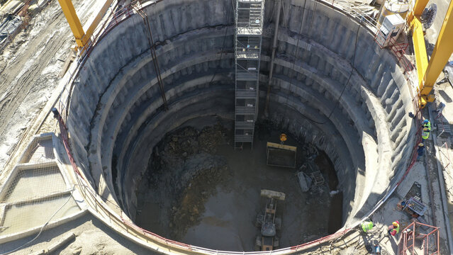 Aerial view of a deep circular construction shaft with reinforced concrete walls, a metal staircase, and an excavator at the bottom Avcilar, Istanbul, Turkiye.