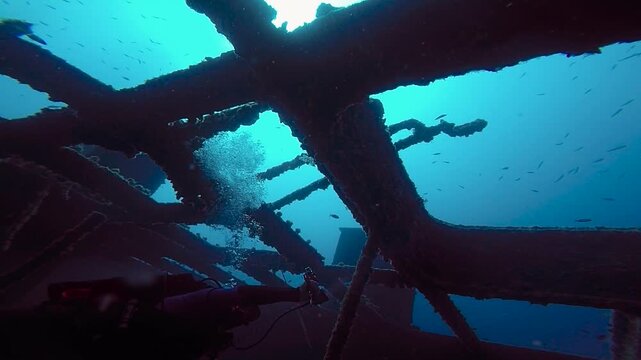 Low Angle View of Diver Levitating in Sunken Ship Skeleton at 40m. Movie-like slow motion showing a scuba diver levitating inside the skeletal metal carcass of a massive shipwreck.  Wreck diving. 