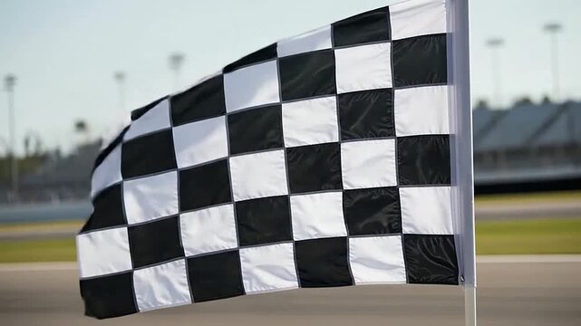 A black and white checkered flag waves in the wind at a sports track