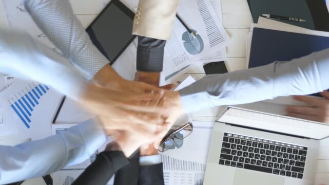 Top view to hands of business people celebrating achievement. Group of employers stacked arms together one by one in unity showing joyful. Creative team working at modern office. Success concept