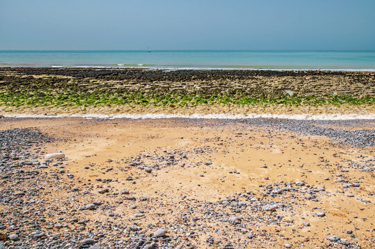 Birling Gap East Sussex Calm Rocky Beach With Sandy Shore, Green Algae Tidal Zone and Distant Sailboat on Turquoise Sea