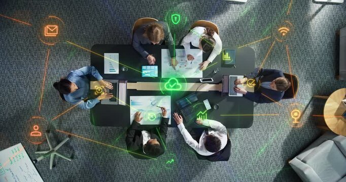 Top Down View of Multiethnic Business Team Meeting Around Boardroom Table With Laptops and Reports as Linked Visualization Layer Appears, Glowing Green Icons Symbolise Cloud Storage and Cybersecurity.