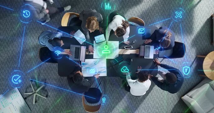 Top Down View of Businesswomen and Businessmen Meeting Around Office Desk With Laptops and Reports as Linked Visualization of Glowing Icons Statistics, Cybersecurity, SAAS and AI.