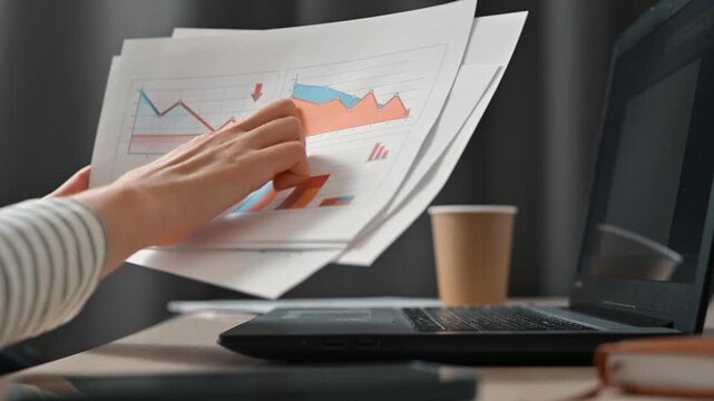 A person is engaged in reviewing and sorting through documents featuring charts and graphs in an office environment