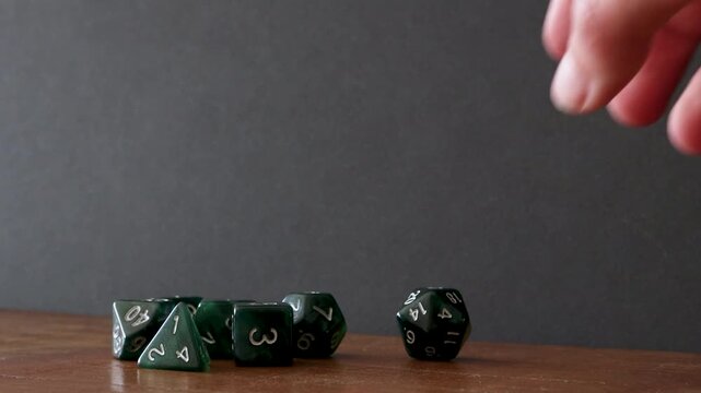 A pile of dice lay on a wooden table, the player first rolls a D20 on the table, picks it up and then rolls it through the frame from right to left until it dissapears out of the frame.