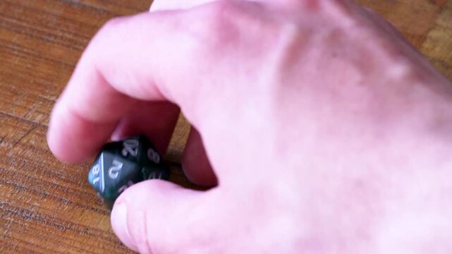 A player rolls a D20 and lands a natural 20 on a wooden table, after a few seconds the player picks up the dice again.