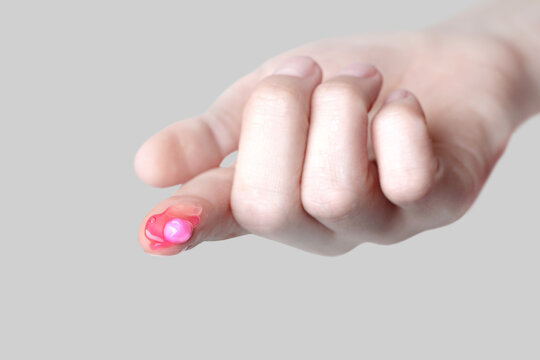 Popular pink capsule face cream on finger, close up grey background
