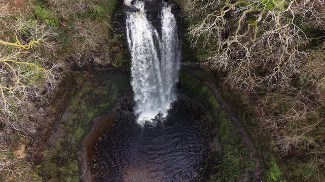 4K aerial video showing Henrhyd Waterfalls with water dropping over a steep rock face surrounded by green woodland.