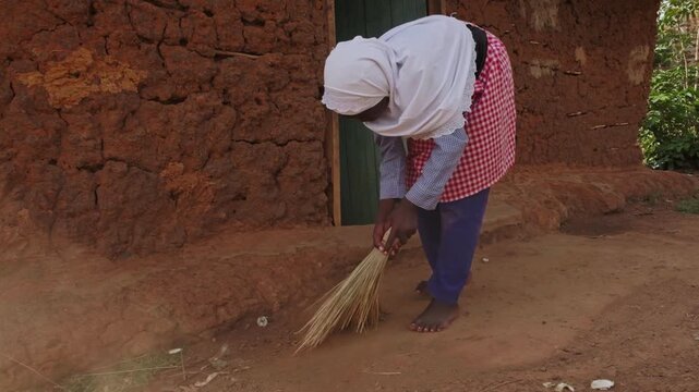 African girl sweeping the ground outside a traditional mud house, showing daily household chores, family support and authentic rural village life in Africa.