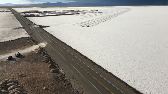 Aerial view of Salinas Grandes salt flats with a straight asphalt road, mining facilities, and dark clouds on the horizon Tumbaya, Jujuy, Argentina.