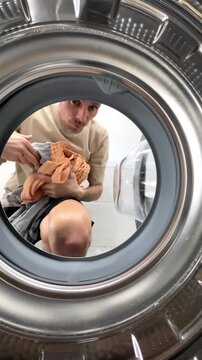 A unique perspective from inside a washing machine: a man takes clean, washed laundry out of the washing machine drum