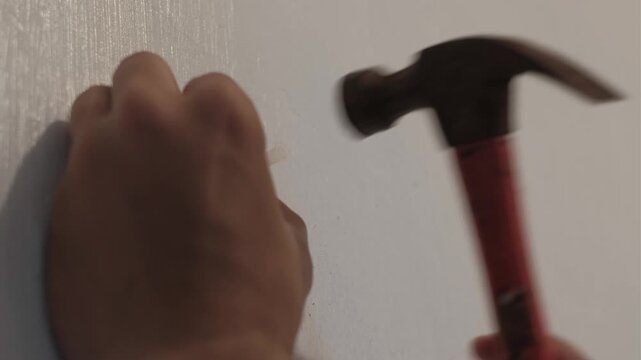 Close-up static shot of a hand hammering a plastic anchor into an interior wall during indoor installation work