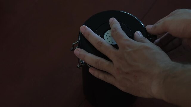 Close-up static shot of hands closing a metal coffee bean canister and setting the storage date on the lid indoors