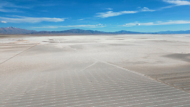 Aerial view of the vast Salinas Grandes salt flats with geometric extraction patterns and distant mountains under a blue sky in Tumbaya, Jujuy, Argentina.