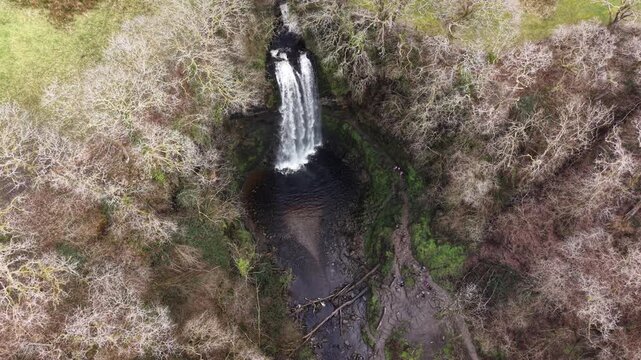 4K drone footage showing Henrhyd Waterfalls surrounded by a forested valley and green terrain.