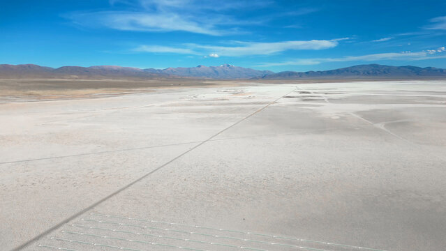 Aerial view of Salinas Grandes salt flats with a straight road stretching towards distant mountains under a blue sky Tumbaya, Jujuy, Argentina.